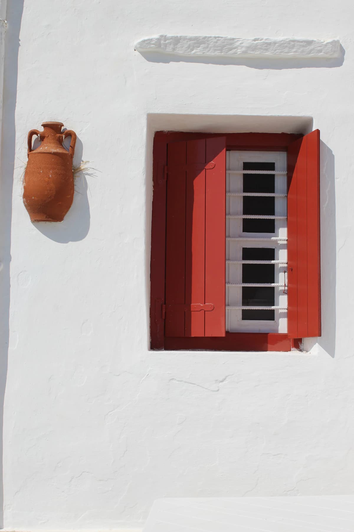 A red-shuttered window in a whitewashed island wall